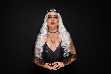 blonde woman in witch crown and veil looking at camera isolated on blackの写真素材