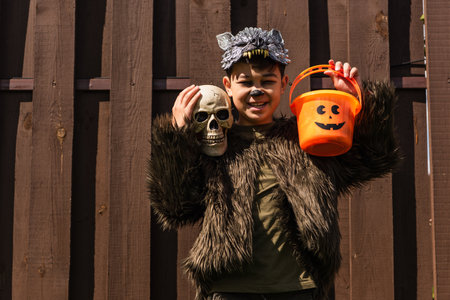 cheerful asian boy in werewolf costume holding skull and halloween bucketの写真素材