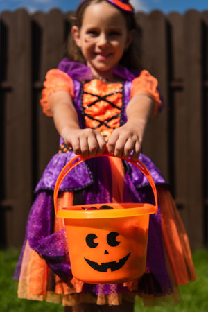 selective focus of trick or treat bucket in hands of girl in clown costume smiling on blurred backgroundの写真素材