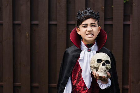 asian boy in vampire king costume growling while holding skull and looking at cameraの写真素材