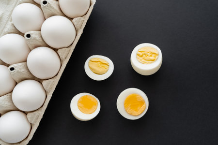 Top view of boiled and raw eggs in cardboard container on black surface