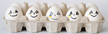 Painted eggs with facial expression and ukrainian flag in container on white background, banner