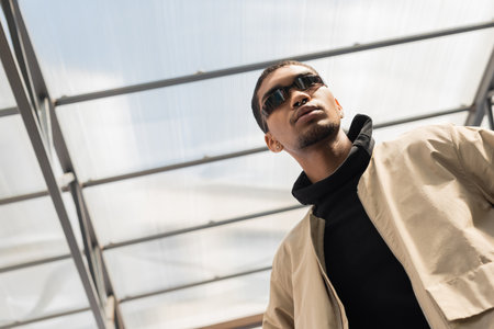 low angle view of african american in stylish sunglasses standing under roofの写真素材