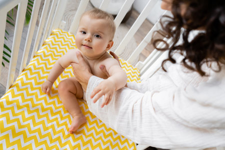 Woman putting baby daughter in crib at home
