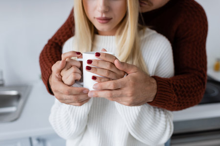 cropped view of young man hugging blonde woman with cup of teaの写真素材