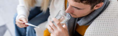 top view of sick man drinking water near woman holding digital thermometer, banner