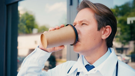 doctor in white coat drinking coffee from paper cup outdoors