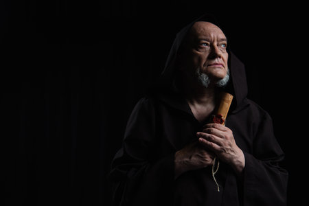 senior monk holding manuscript with wax seal and looking away isolated on blackの写真素材