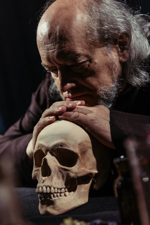 senior medieval philosopher leaning on skull while thinking isolated on black