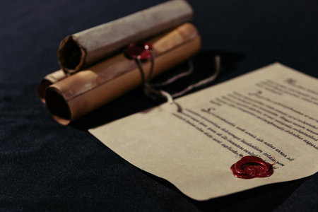 old manuscript stamped with wax seal near rolled parchments on black backgroundの写真素材