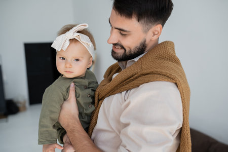 cheerful bearded father holding in arms baby girl in dress and headbandの写真素材