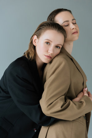 pretty lesbian woman looking at camera and embracing lesbian girlfriend standing with closed eyes...