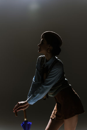 silhouette of young woman in beret and autumnal outfit on dark grey background