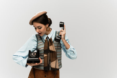 amazed young woman in beret holding vintage telephone isolated on greyの写真素材