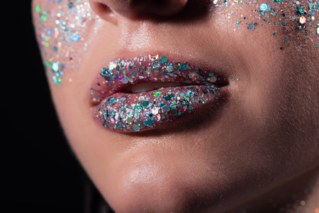 cropped view of young woman with sparking glitter on lips isolated on blackの写真素材