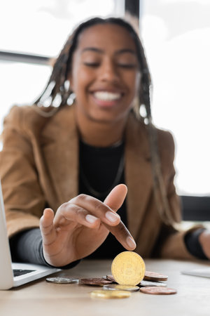 KYIV, UKRAINE - APRIL 27, 2022: Blurred african american businesswoman touching bitcoin near laptop...