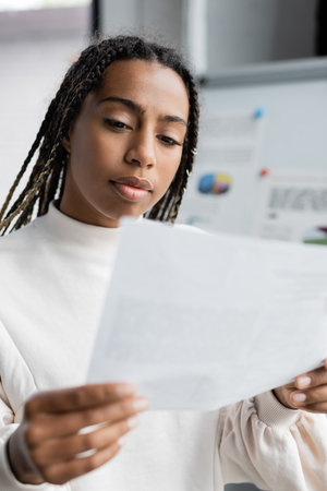 African american businesswoman holding document near blurred flip chair in officeの写真素材