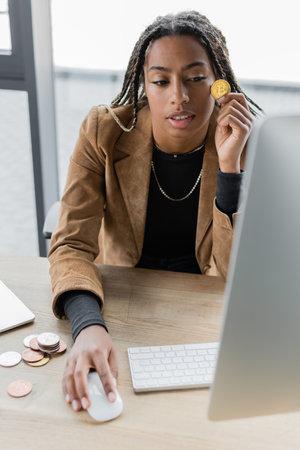 African american businesswoman holding bitcoin and using computer in office