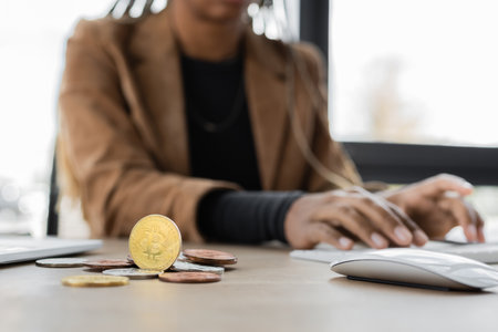 Cropped view of bitcoins near blurred african american businesswoman typing on computer keyboard