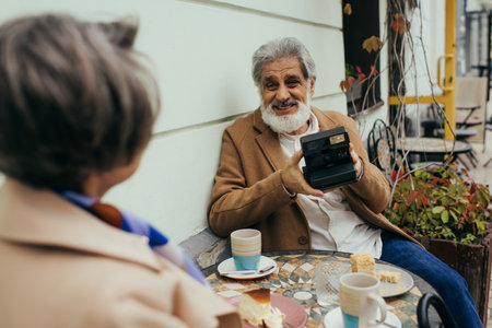 happy senior man with beard holding vintage camera during breakfast with wifeの写真素材