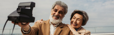 happy senior man taking selfie with cheerful wife on vintage camera, banner