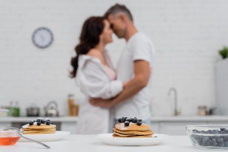 Pancakes with blueberries near blurred couple kissing in kitchenの写真素材