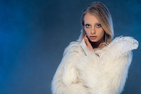 pierced woman with snow on hair and white eyebrows posing on dark blue