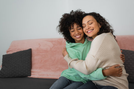 happy african american mother and daughter hugging while sitting on couchの写真素材