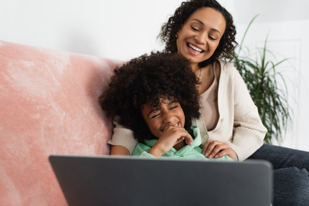 happy african american mother and daughter watching comedy movie on laptopの写真素材
