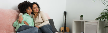 happy african american mother hugging cheerful preteen daughter in living room, banner