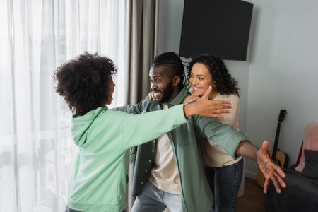 happy african american girl hugging cheerful parents at homeの写真素材