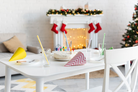 Birthday cake near glasses and party caps on table in living roomの写真素材