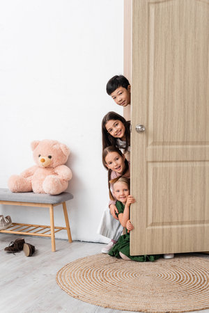 Happy multiethnic children looking at camera near open door in hallway at homeの写真素材