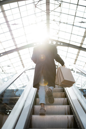 back view of african american man with shopping bags walking on escalator in sunshineの写真素材