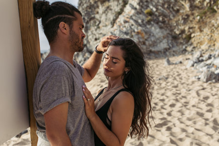 bearded man adjusting wavy hair of girlfriend on beach in portugalの写真素材