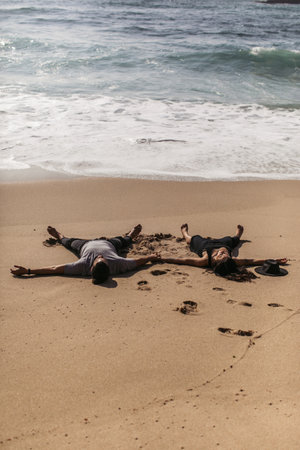 couple lying on wet sand near ocean on beach in portugalの写真素材