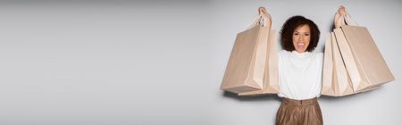 excited african american woman in autumnal outfit holding shopping bags on grey, bannerの写真素材