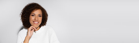 portrait of happy and curly african american woman smiling on grey background, banner