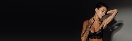 young tattooed woman in sexy bra posing on black and grey background, bannerの写真素材