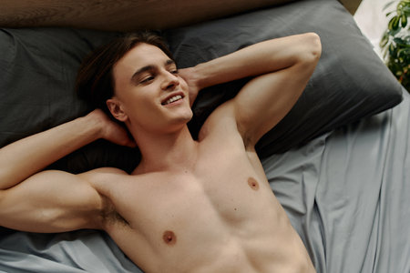 top view of smiling and sexy man lying on black pillows with hands behind head and looking awayの写真素材