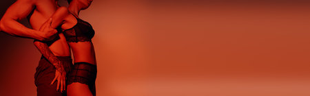 side view of woman in black sexy underwear near shirtless man on red background, bannerの写真素材