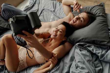 Top view of smiling woman in lingerie taking selfie with shirtless boyfriend on bedの写真素材