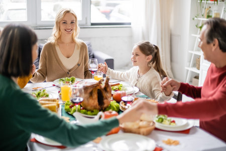 Smiling woman looking at camera while family holding hands near thanksgiving dinner at homeの写真素材