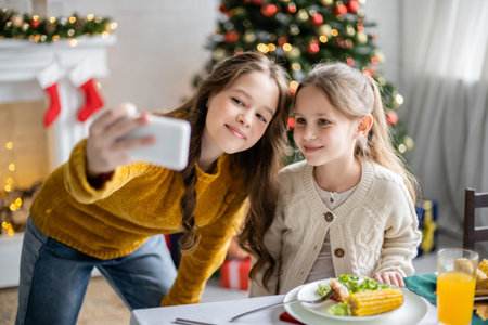 Smiling sisters taking selfie on smartphone during thanksgiving dinner at homeの写真素材