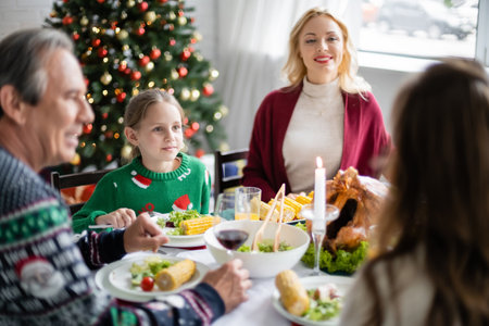 cheerful woman looking at family during festive dinner near christmas treeの写真素材