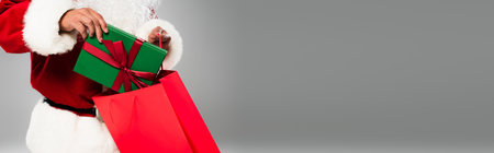 Cropped view of father christmas putting gift in shopping bag isolated on grey, bannerの写真素材