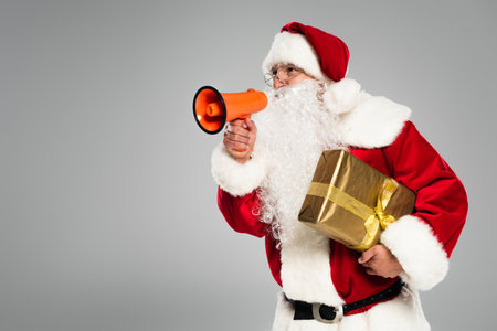 Santa claus in eyeglasses holding loudspeaker and present isolated on greyの写真素材
