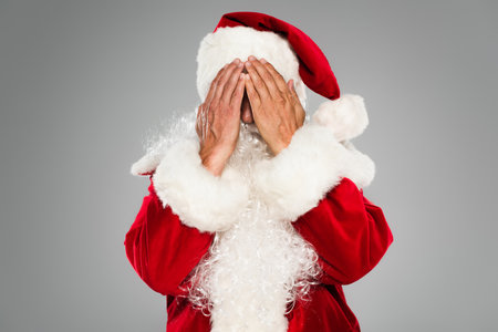Bearded santa claus in costume covering face isolated on greyの写真素材