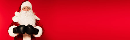 Father christmas in costume and boxing gloves on red background with copy space, bannerの写真素材