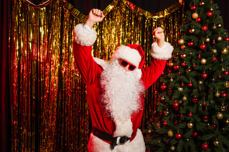 Father christmas in sunglasses dancing during party near pine tree and tinselの写真素材